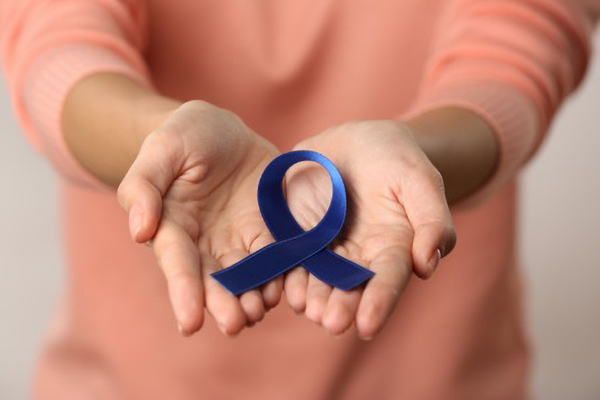 blue ribbon in hands representing bowel cancer article by Lesley Lyle